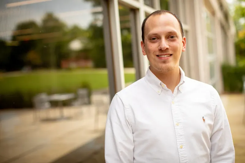 Duncan Lord smiling in a white button-down shirt outside a glass-walled building